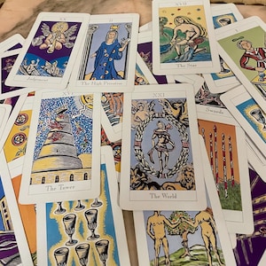 May include: A collection of tarot cards with various illustrations and titles. The cards feature images of figures, symbols, and scenes, including "The High Priestess," "The Tower," and "The World." The color palette includes blues, yellows, purples, and oranges.