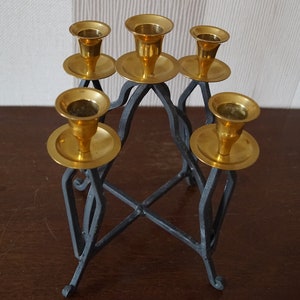 May include: A black metal candelabra with five gold candle holders. The candelabra has a geometric design and is perfect for holding candles.