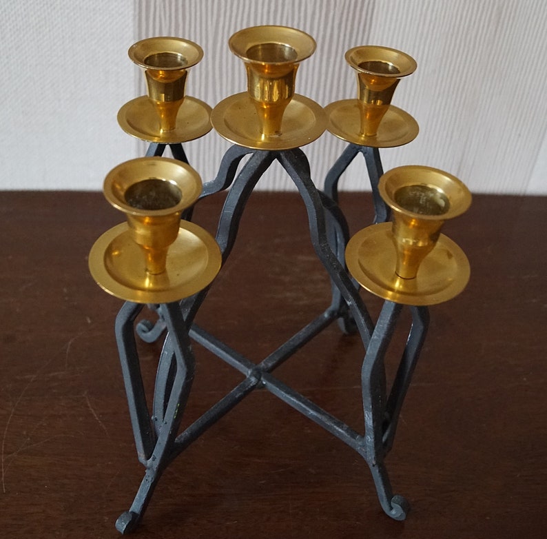 May include: A black metal candelabra with five gold candle holders. The candelabra has a geometric design and is perfect for holding candles.