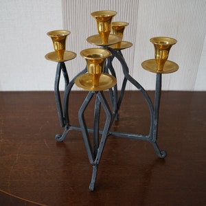 May include: A black metal candelabra with five gold candle holders. The candelabra has a geometric design and a sturdy base.