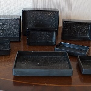 May include: A set of eight black rectangular boxes of varying sizes, arranged on a wooden surface.