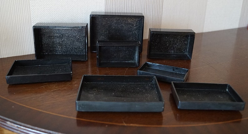 May include: A set of eight black rectangular boxes of varying sizes, arranged on a wooden surface.