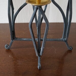May include: Black metal candle holder with a geometric design and three legs. The holder has a brass top for a candle.