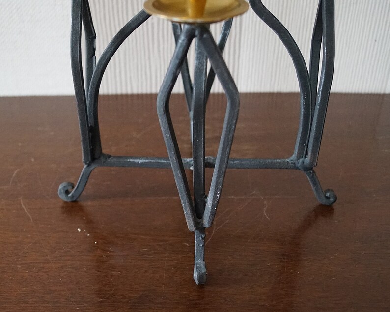 May include: Black metal candle holder with a geometric design and three legs. The holder has a brass top for a candle.