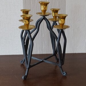 May include: A black metal candelabra with five gold candle holders. The candelabra has a geometric design and a sturdy base.