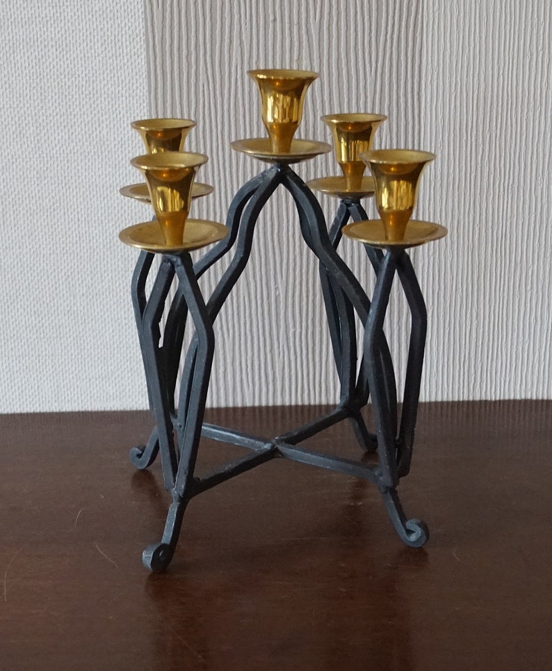 May include: A black metal candelabra with five gold candle holders. The candelabra has a geometric design and a sturdy base.