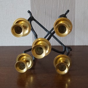 May include: A black metal candelabra with five gold candle holders. The candelabra is designed in a criss-cross pattern.