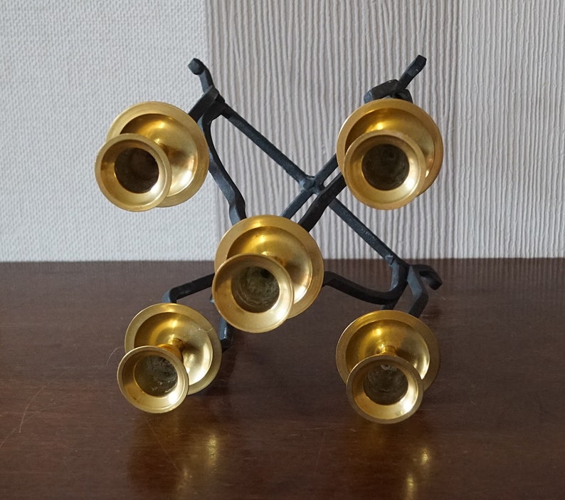 May include: A black metal candelabra with five gold candle holders. The candelabra is designed in a criss-cross pattern.