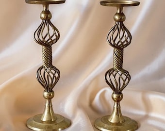 Può includere: Una coppia di candelabri in ottone abbinati con base circolare, uno stelo centrale con due sezioni a gabbia aperta, una parte centrale in metallo intrecciato e una piastra superiore circolare piatta per sostenere una candela.
