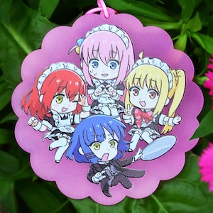 Puede incluir: Un dije rosa con borde festoneado que presenta un grupo de personajes de estilo anime con trajes de doncella. El dije está rodeado de hojas verdes y vibrantes flores rosas, creando una escena colorida y alegre.