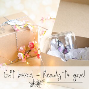 May include: A gift box with a glass cloche containing a butterfly decoration. The cloche sits in a cardboard box with white tissue paper. The image includes the text "Gift boxed - Ready to give!" and is decorated with pink flowers.