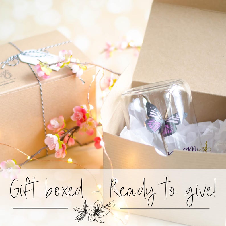 May include: A gift box with a glass cloche containing a butterfly decoration. The cloche sits in a cardboard box with white tissue paper. The image includes the text "Gift boxed - Ready to give!" and is decorated with pink flowers.