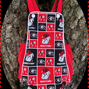 May include: Red and black baby onesie with a white trim. The onesie has a checkered pattern with the University of Georgia logo and a bulldog mascot.