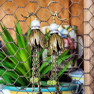 May include: A pair of gold tone earrings with a flower design and a pearl and green bead accents. The earrings hang from a chain with a cross charm.