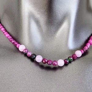 Puede incluir: Un collar de piedras preciosas rosa, morado y verde con un patrón de color degradado. El collar está hecho de cuentas facetadas y está enhebrado en un cordón delgado.