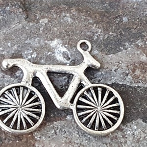 May include: A silver charm in the shape of a bicycle. The bicycle has a detailed design with spokes on the wheels.