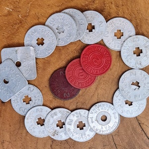 May include: A collection of round, silver tokens with various text and designs, including the words "Colorado Sales Tax" and "Consumer's Tax." There are also several red tokens with the words "Colorado Sales Tax" and the number "2" on them.