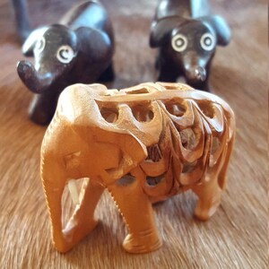 May include: Three wooden elephant figurines. Two are dark brown and one is light brown with intricate carvings. The light brown elephant is in focus and the other two are out of focus.