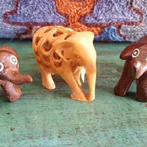 May include: Three wooden elephant figurines. One is carved with intricate details and painted brown, while the other two are painted brown with white eyes.