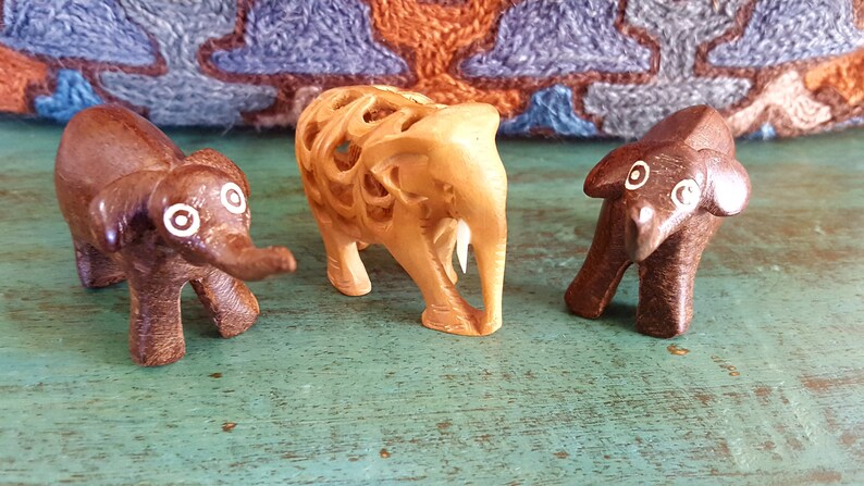 May include: Three wooden elephant figurines. One is carved with intricate details and painted brown, while the other two are painted brown with white eyes.