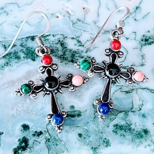 May include: A pair of silver cross earrings featuring black, red, green, and blue gemstones. The earrings have an intricate design and are ideal for adding a touch of sophistication to any outfit.