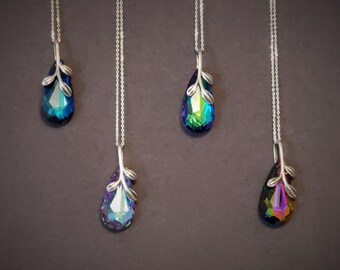 May include: Four silver pendant necklaces with teardrop-shaped, iridescent crystals. Each pendant has a silver leaf design at the top. The crystals display a range of colors, including blue, green, purple, and pink, reflecting light.