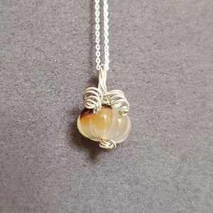 May include: A silver chain necklace with a brown and white agate gemstone pendant. The pendant is wrapped in silver wire to resemble a pumpkin.