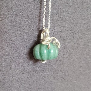 May include: A silver chain necklace with a green jade pumpkin pendant. The pumpkin is carved with ridges and has a silver wire stem.