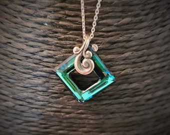May include: A silver chain necklace with a green square pendant featuring a swirl design. The pendant has a faceted, iridescent finish.