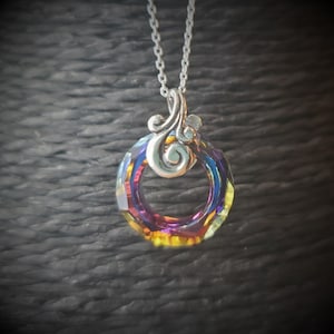 May include: A silver necklace featuring a pendant with a faceted, iridescent crystal ring. The crystal displays a spectrum of colors, including purple, blue, and yellow. The pendant is connected to a delicate silver chain.