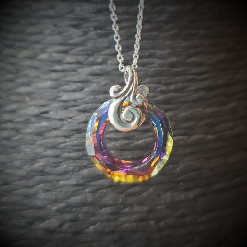 May include: A silver necklace featuring a pendant with a faceted, iridescent crystal ring. The crystal displays a spectrum of colors, including purple, blue, and yellow. The pendant is connected to a delicate silver chain.