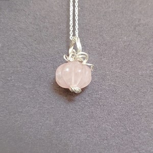 May include: A delicate silver chain necklace with a pink rose quartz pumpkin pendant.