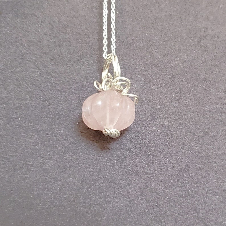 May include: A delicate silver chain necklace with a pink rose quartz pumpkin pendant.