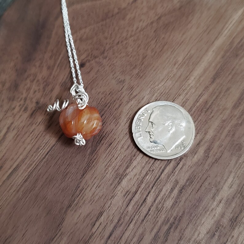 May include: A silver chain necklace with a brown carnelian stone pendant wrapped in silver wire. The pendant is about the size of a dime.