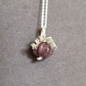 May include: A silver chain necklace with a purple gemstone pendant wrapped in silver wire.