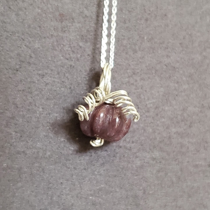 May include: A silver chain necklace with a purple gemstone pendant wrapped in silver wire.