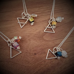 May include: Four silver necklaces with triangle pendants and colorful crystal beads. Each necklace features a different color combination of crystals, including red, orange, yellow, green, blue, and clear.