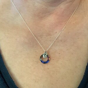 May include: A silver necklace with a pendant featuring a colorful, circular design. The pendant has a swirling, decorative top element and a vibrant mix of blue, red, and orange hues within the circle. The necklace is worn on a person.