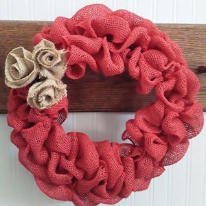 Könnte beinhalten: Ein roter Burlap-Kranz mit drei braunen Burlap-Rosetten.