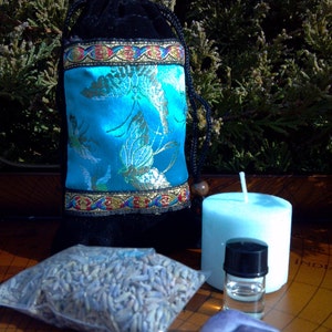 Puede incluir: Una bolsa de terciopelo azul con ribetes dorados y un diseño floral azul y dorado, una pequeña bolsa de lavanda seca, una botella de vidrio transparente con tapa negra, una vela azul claro y una piedra de amatista púrpura.