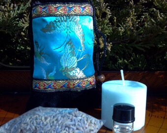 May include: A blue velvet pouch with gold trim and a blue and gold floral design, a small bag of dried lavender, a clear glass bottle with a black lid, a light blue candle, and a purple amethyst stone.