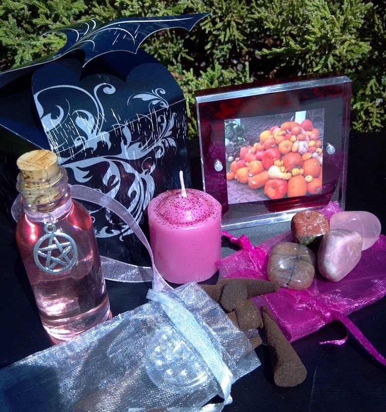 May include: A witchy gift set with a black box, a pink candle, a bottle of pink liquid with a pentagram charm, a small bag of incense, and a frame with a picture of pumpkins.