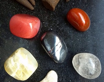 May include: An assortment of polished gemstones in red, orange, yellow, clear, and metallic gray hues. Several brown incense cones are arranged at the top. The stones vary in shape and size, with a coral-like piece at the bottom.