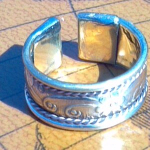 May include: Silver toe ring with a decorative design of swirling lines and a rope-like border.