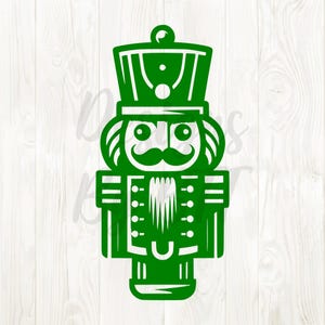 May include: A green, stylized illustration of a nutcracker soldier. The design features a detailed hat, mustache, and uniform, with a decorative, festive appearance. The image is set against a white wooden background.