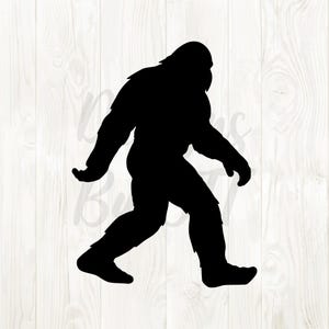 May include: Black silhouette of Bigfoot walking to the right. The creature is depicted with a large, hairy body, a prominent brow, and long arms. The background is a light wood grain pattern.