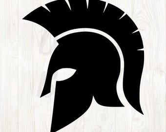 May include: A black silhouette of a Spartan helmet, featuring a crest and cheek guards. The helmet is a classic symbol of ancient Greek warriors, rendered in a simple, bold design. The image is set against a white wooden background.