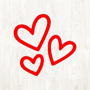 May include: Three red heart shapes on a white wooden background. The hearts are drawn with a thick outline, creating a simple and bold design. The hearts vary in size and are arranged in a cluster.