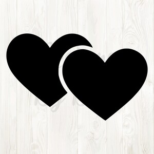 Puede incluir: Dos formas de corazón negras superpuestas sobre un fondo blanco con vetas de madera. Los corazones tienen un diseño sólido y sencillo, con bordes redondeados y una silueta de corazón clásica. La imagen es un gráfico o ilustración.