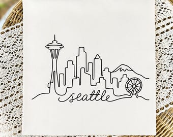 May include: A square white fabric panel featuring a black continuous line drawing of the Seattle skyline. The design includes the Space Needle, various skyscrapers, a mountain silhouette, a Ferris wheel, and the word seattle in cursive script.